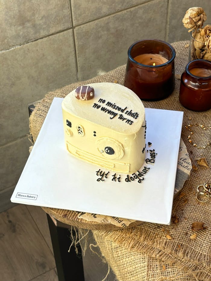 A creative camera-shaped cake displayed with candles on a rustic table setting.