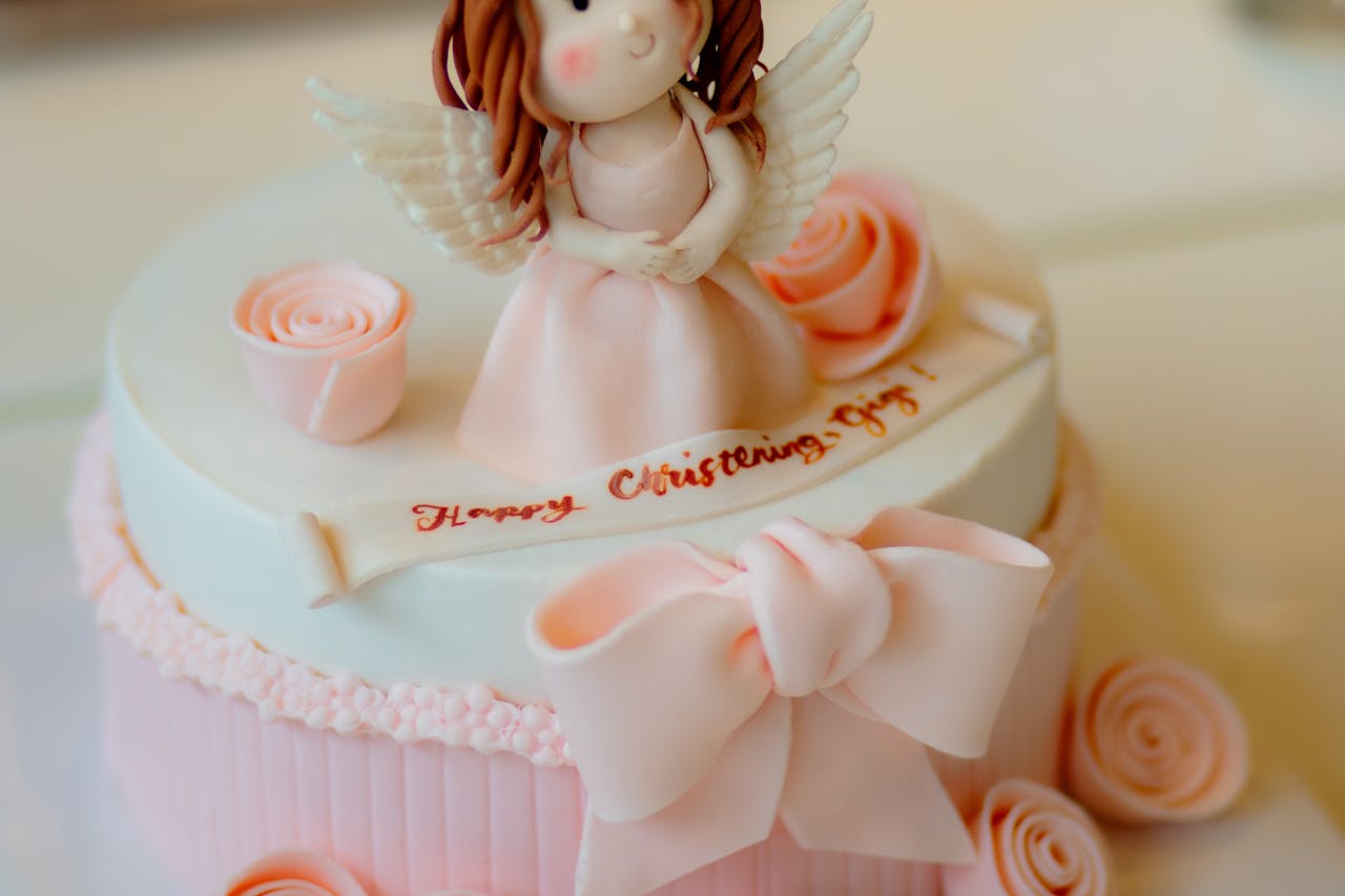Delicate pink christening cake featuring an angel topper and floral decorations, perfect for celebrations.