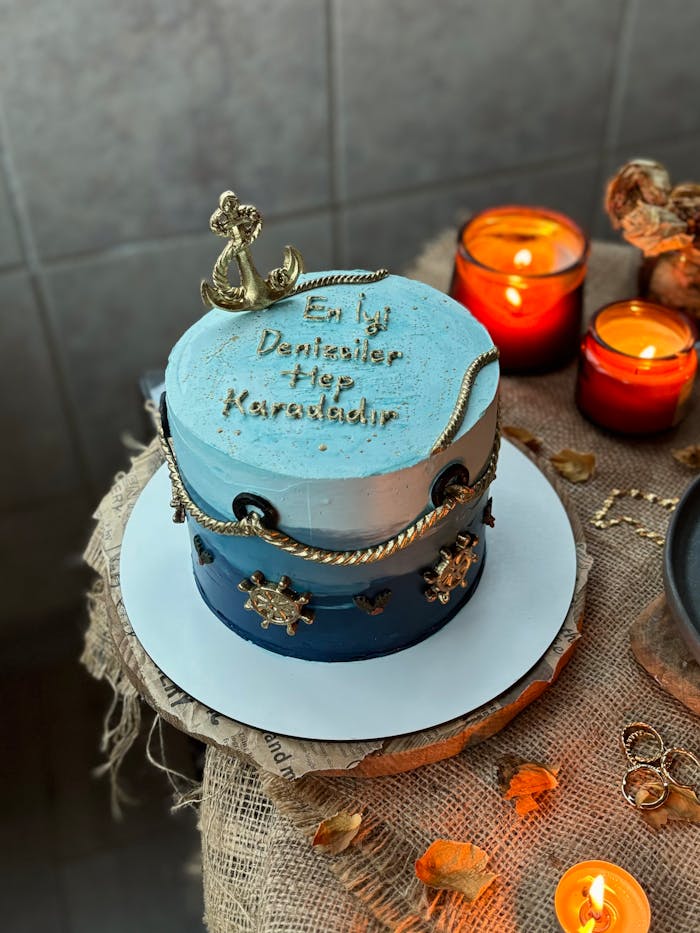 Blue nautical cake with anchor, surrounded by candles on rustic burlap.