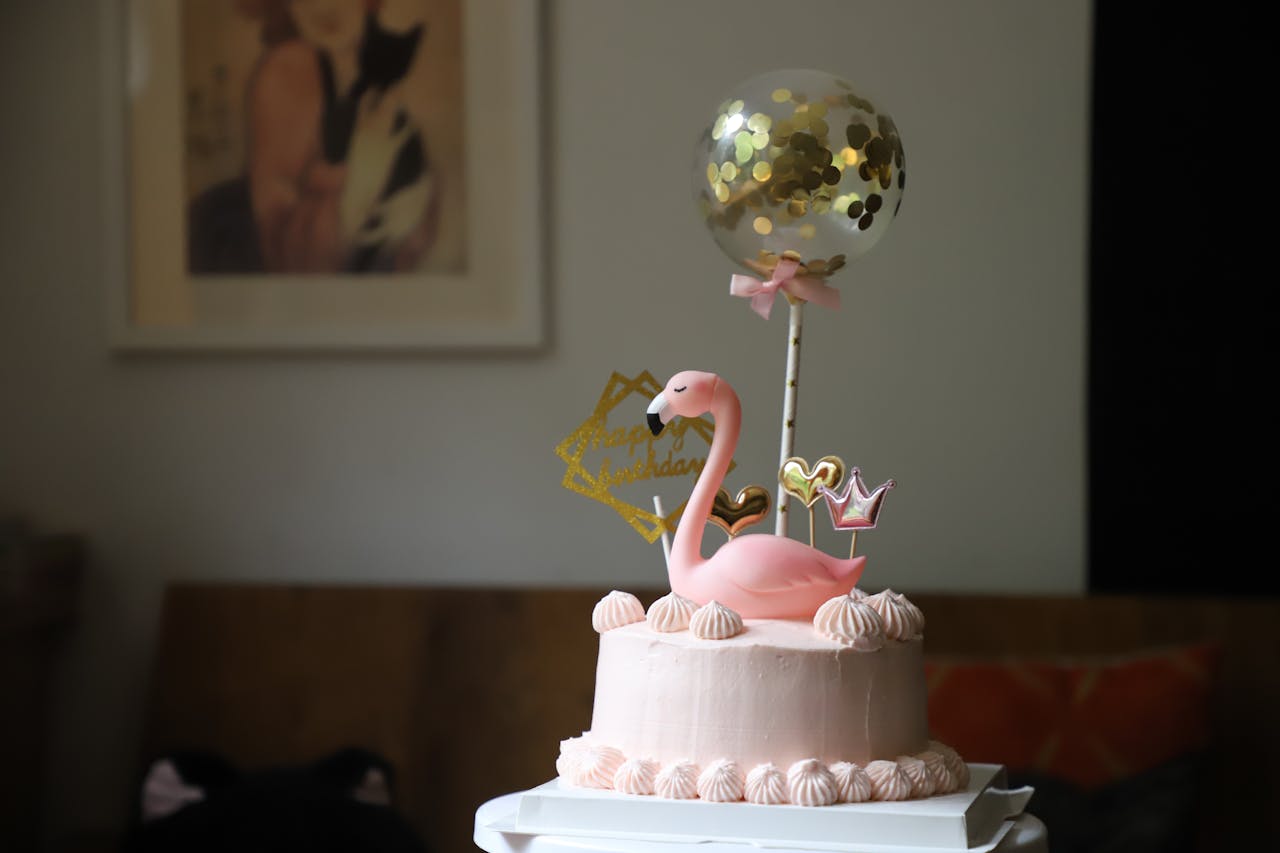 Elegant pink birthday cake with flamingo and balloon decorations indoors.