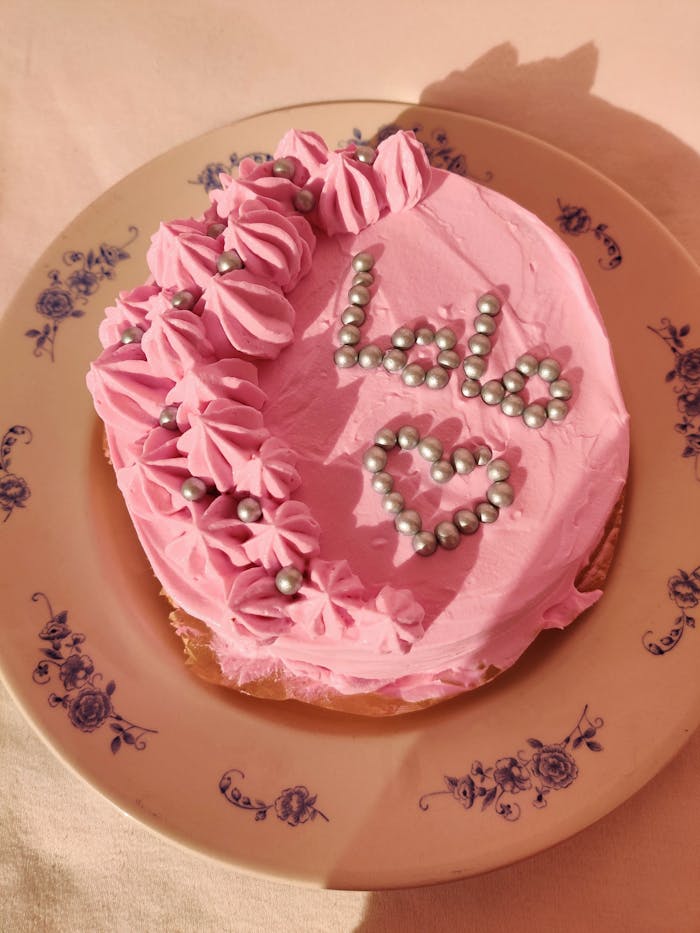 Pink frosted cake with decorative pearls and text Lolo on floral plate.