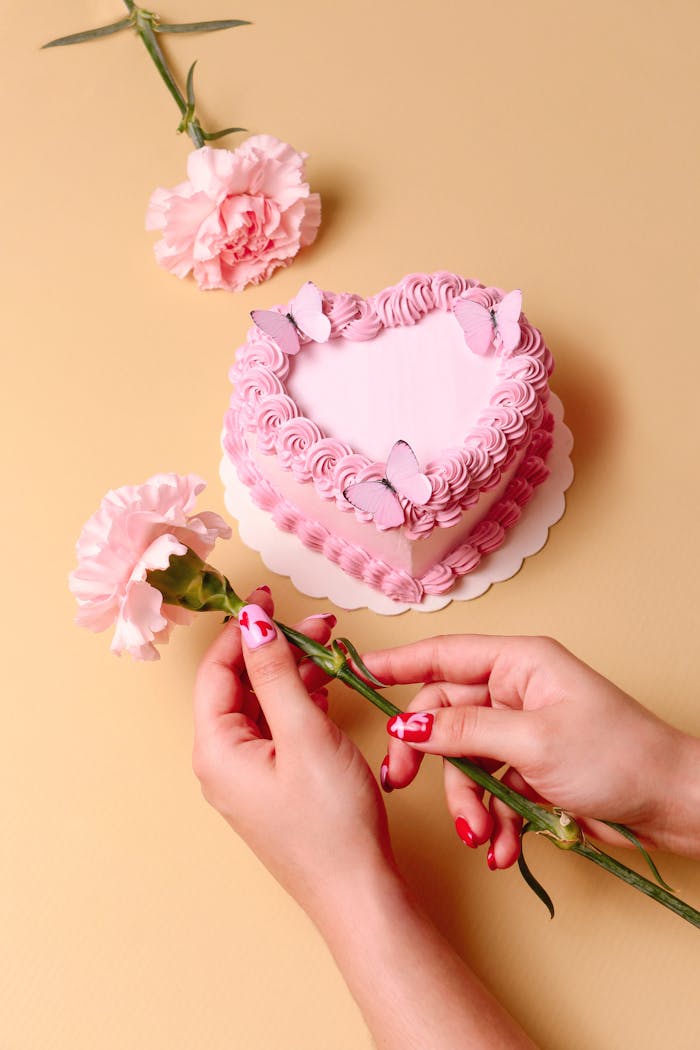 A heart-shaped pink cake with butterflies and a carnation on a yellow background, perfect for celebrations.